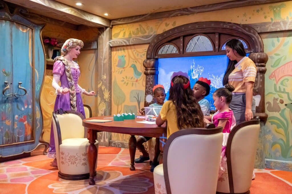 Entre las cosas qué hacer en un crucero de Disney están los clubes de niños. Área de princesas del club de niños, con niños con coronas de papel y Rapunzel interactuando con ellos