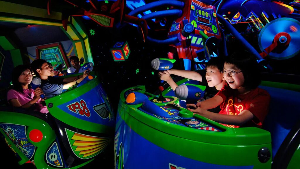 Niños en la atracción Buzz Lightyear sosteniendo las pistolas de rayo laser y apuntando a los blancos. Por ser interactiva esta es una de las mejores atracciones para niños en Disneyland