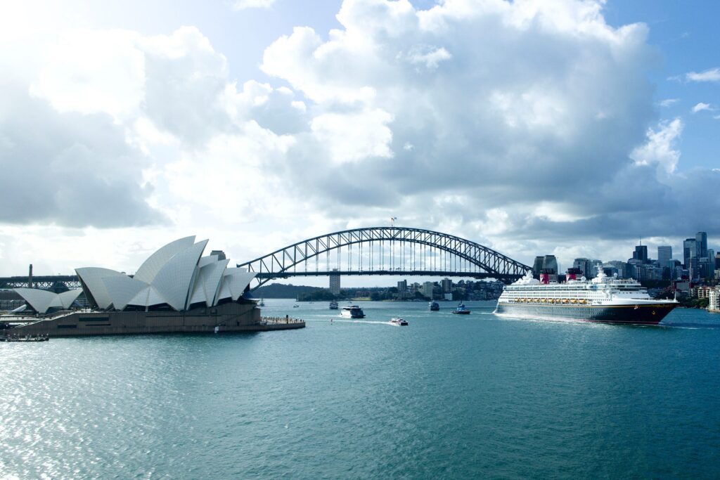 Crucero de Disney pasando a un lado de la Opera de Sydney. Los Itinerarios de Disney Cruise Line en 2024 en Australia te llevarán a otras ciudades como Melbourne